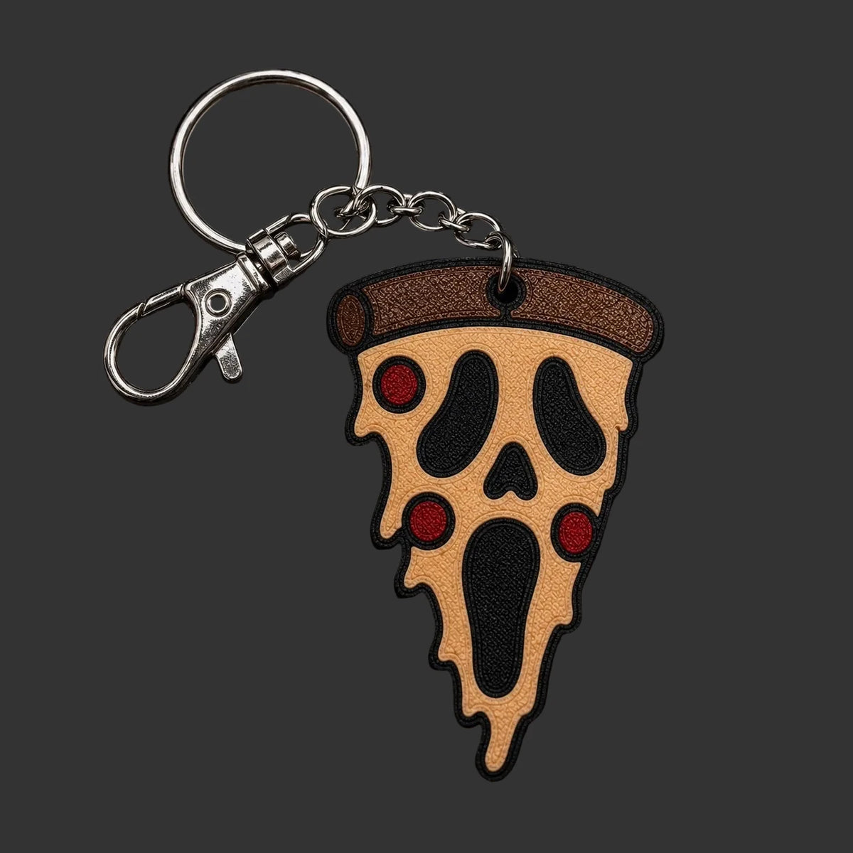 A horror-themed keychain shaped like a slice of pizza with a Ghostface-style face, featuring a silver clasp and resting on a dark stone background.