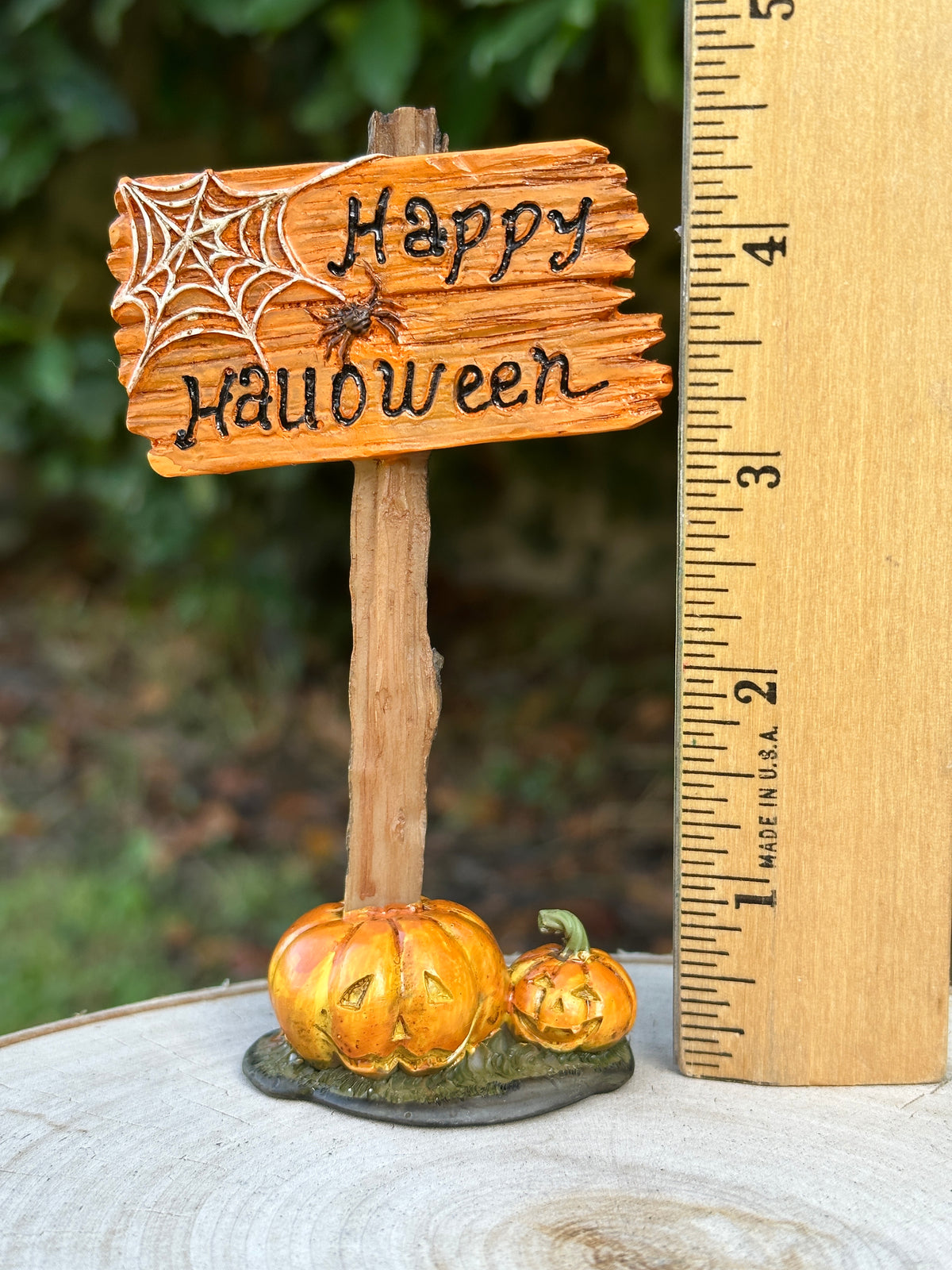 Size reference photo of Happy Halloween sign miniature next to a ruler showing approximately 4.5 inches tall, with jack-o-lanterns and spider web detail