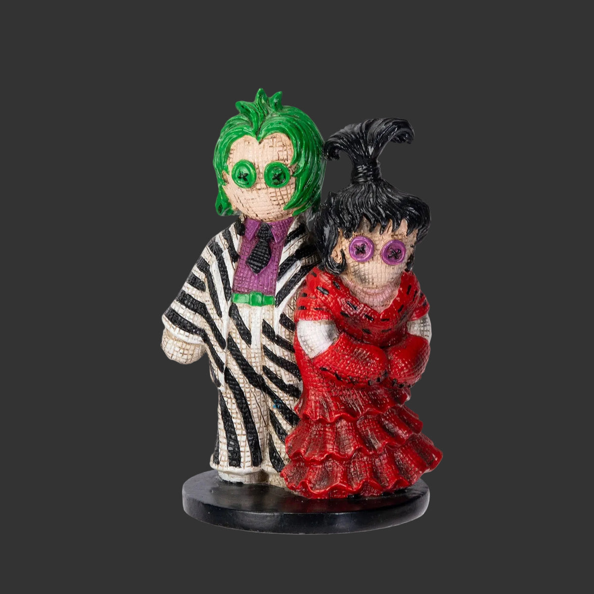 Two stylized Pinhead Monster figures, Beetlejuice and his bride Lydia one with green hair and the other with black hair and a red outfit, on a black background.