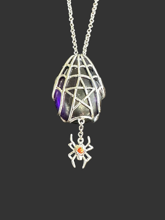 An Anne Stokes gothic-style silver spider pendant necklace featuring a spiderweb cage design, a dark glass vial with purple and green iridescence, and a dangling silver spider charm with a small orange gemstone.