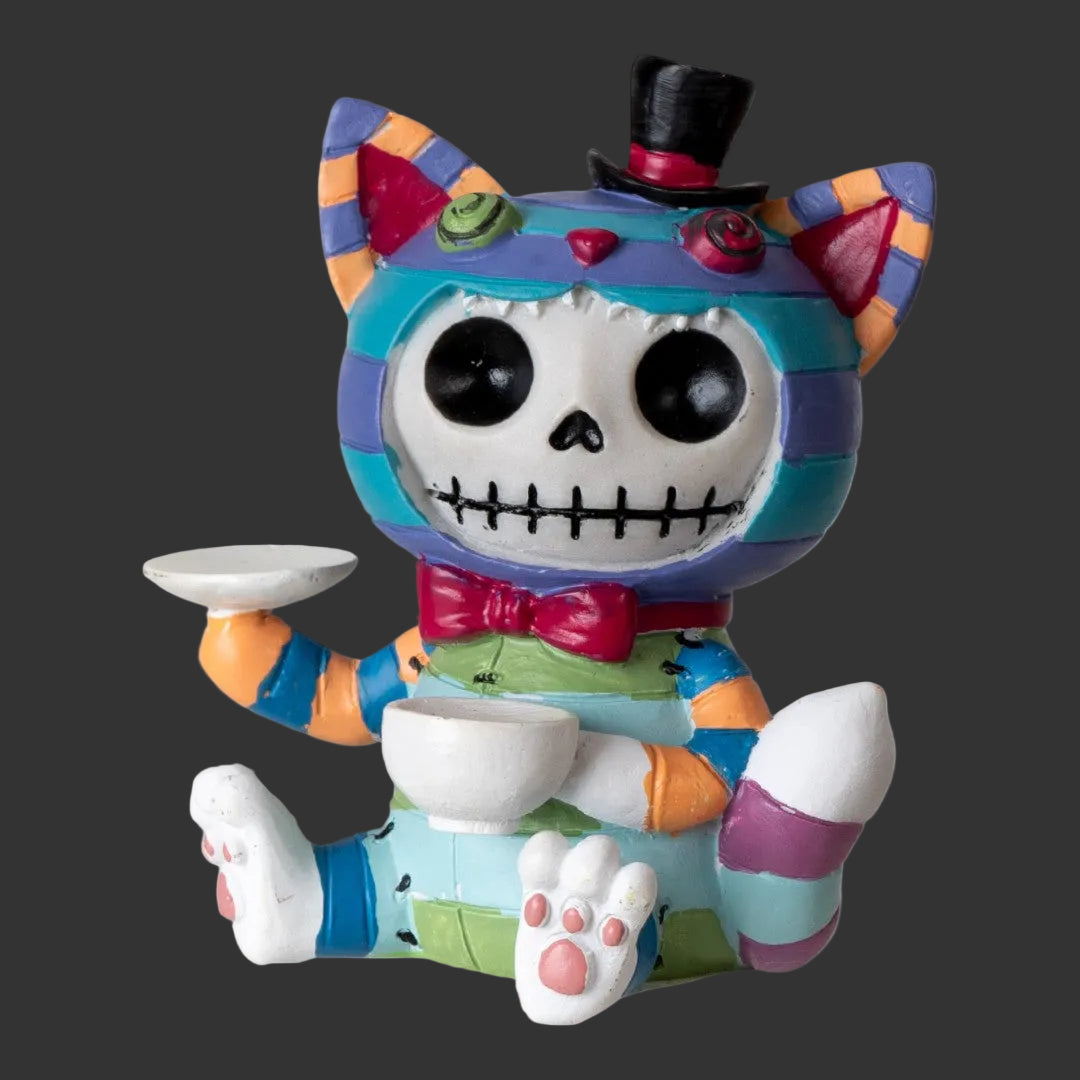 A colorful Alice in Wonderland Chesire cat figurine with a skull face, black top hat, bow tie, striped body, and white teacups in one hand and paw, shown on a black background.