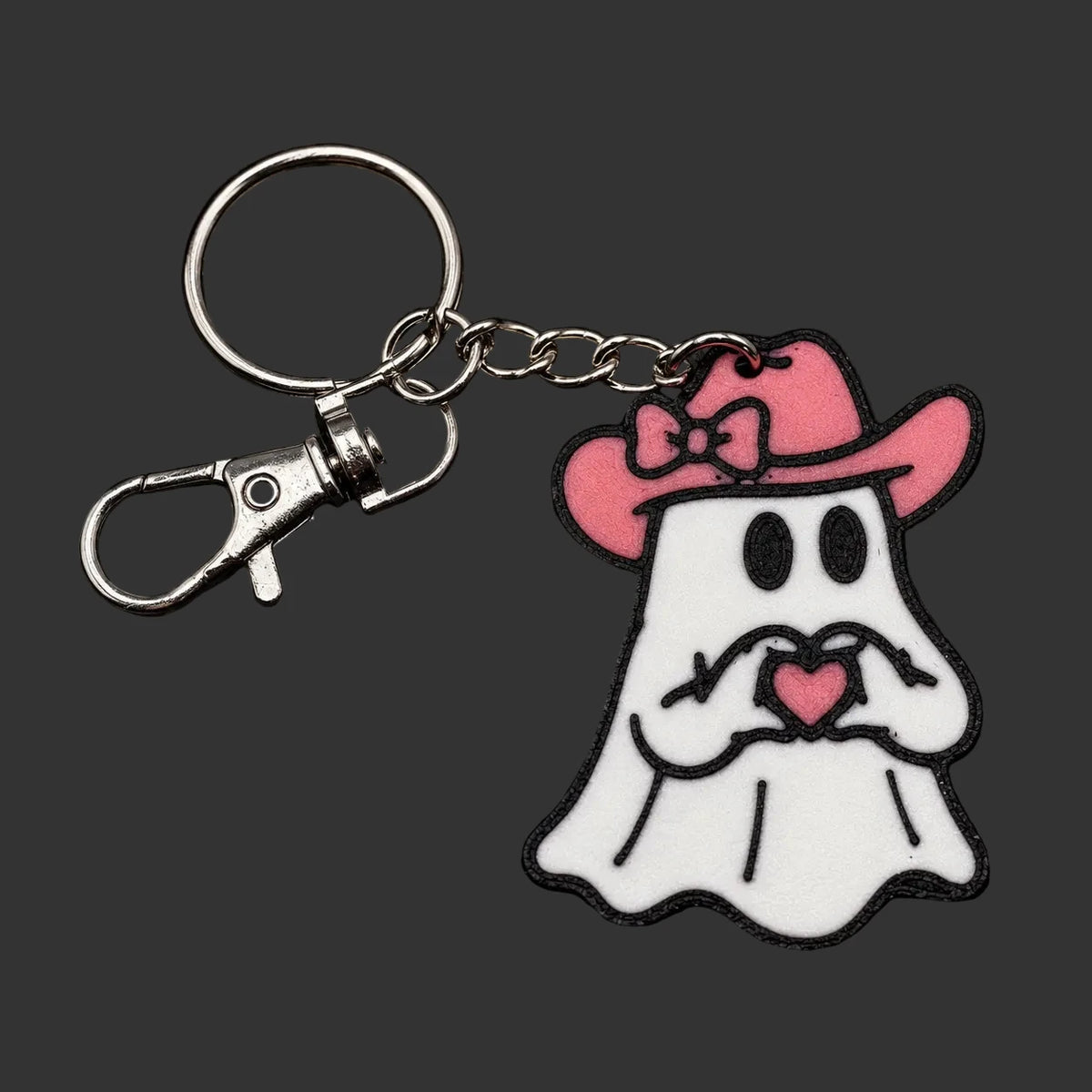Keychain Girly charm with cute ghost host design wearing a pink cowgirl hat and holding a pink on a dark surface