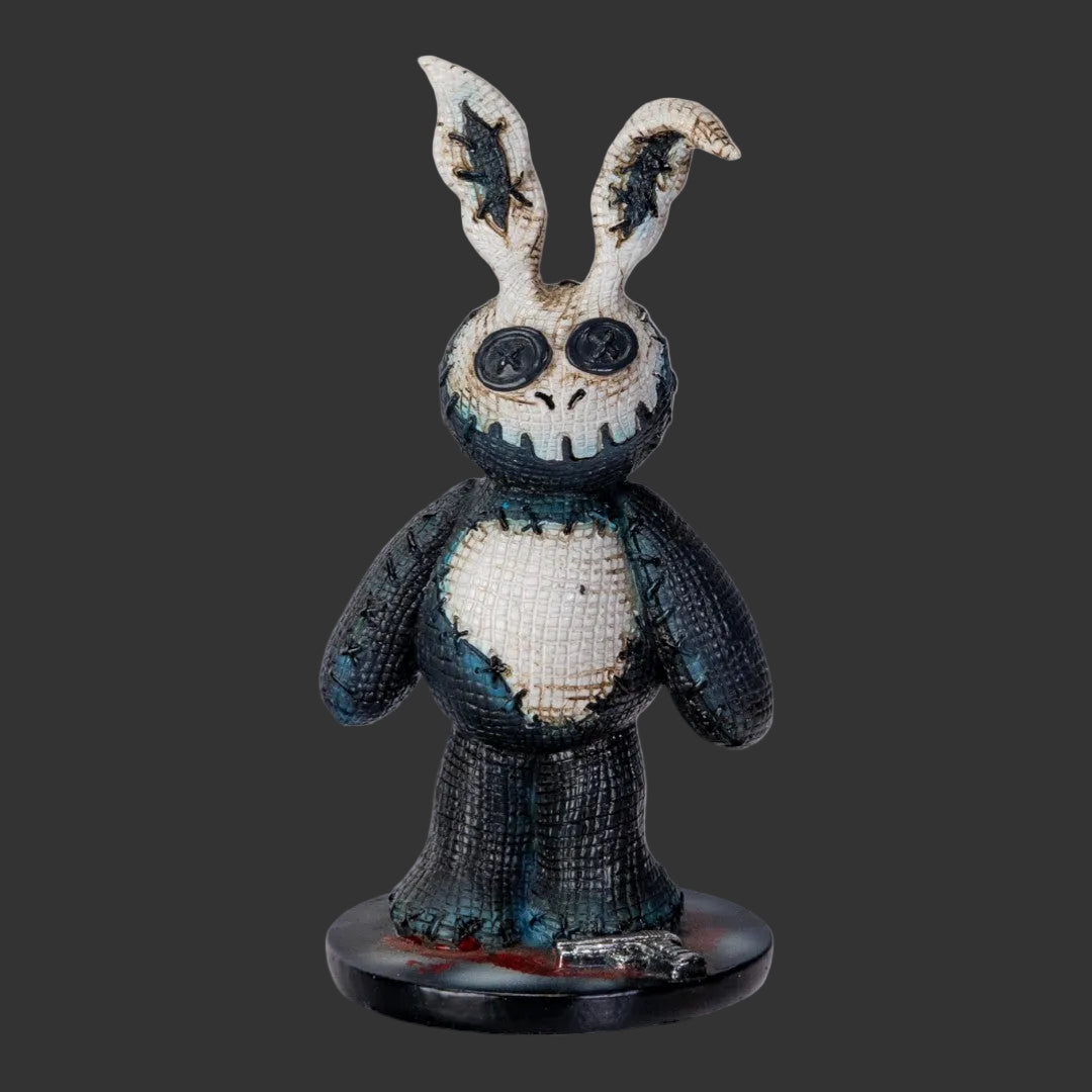 A Pinhead Monster creepy stitched Donnie Darko horror movie bunny figurine with tattered ears, large button eyes, and a stitched mouth, standing on a round base against a black background.