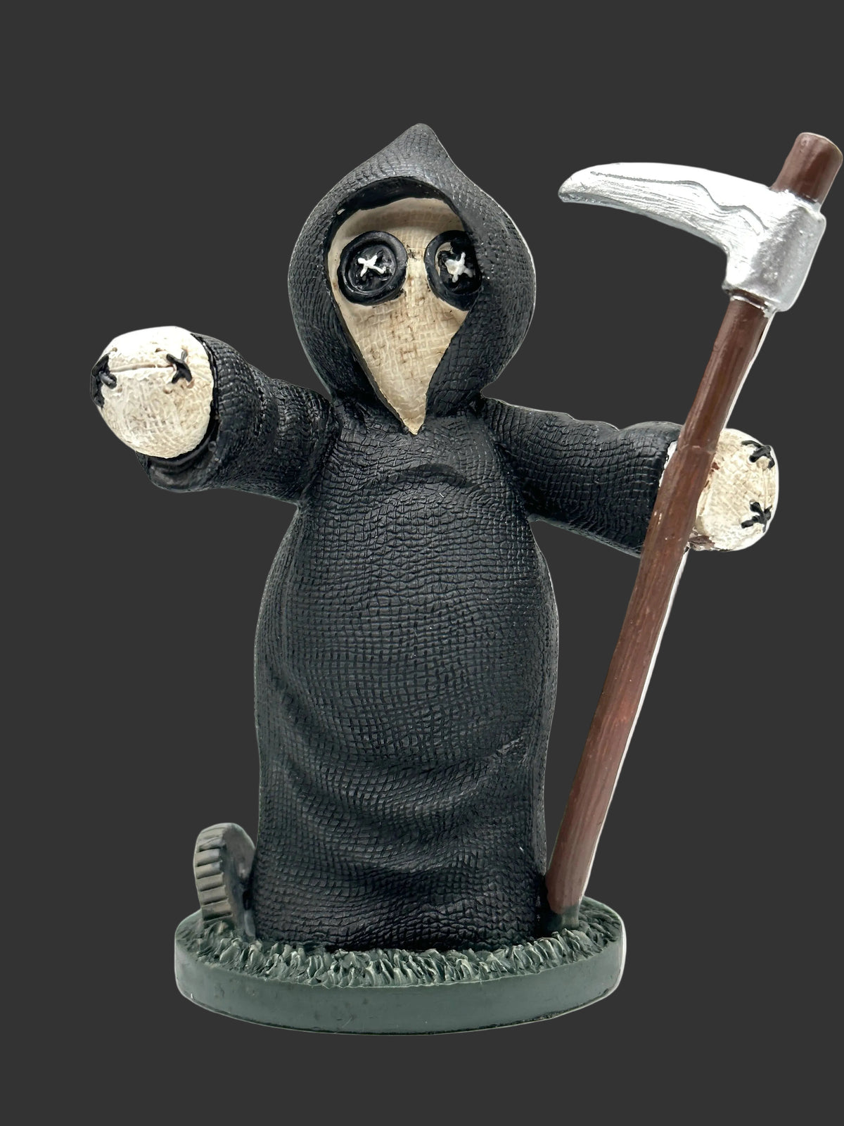 A grim reaper Pinhead Monster figurine wearing a textured black hooded robe and a beige plague mask with black star eyes, holding a scythe with a brown handle and silver blade, standing on a round base against a white background.