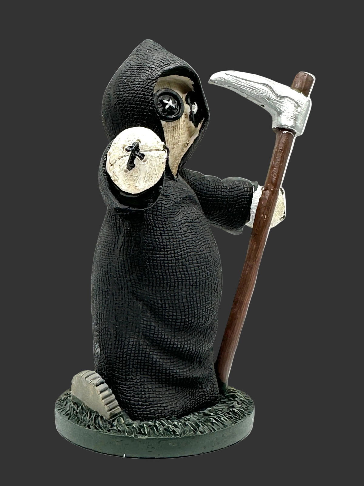 A grim reaper Pinhead Monster figurine wearing a textured black hooded robe and holding a scythe with a silver blade and brown handle, standing on a round dark base against a black background.