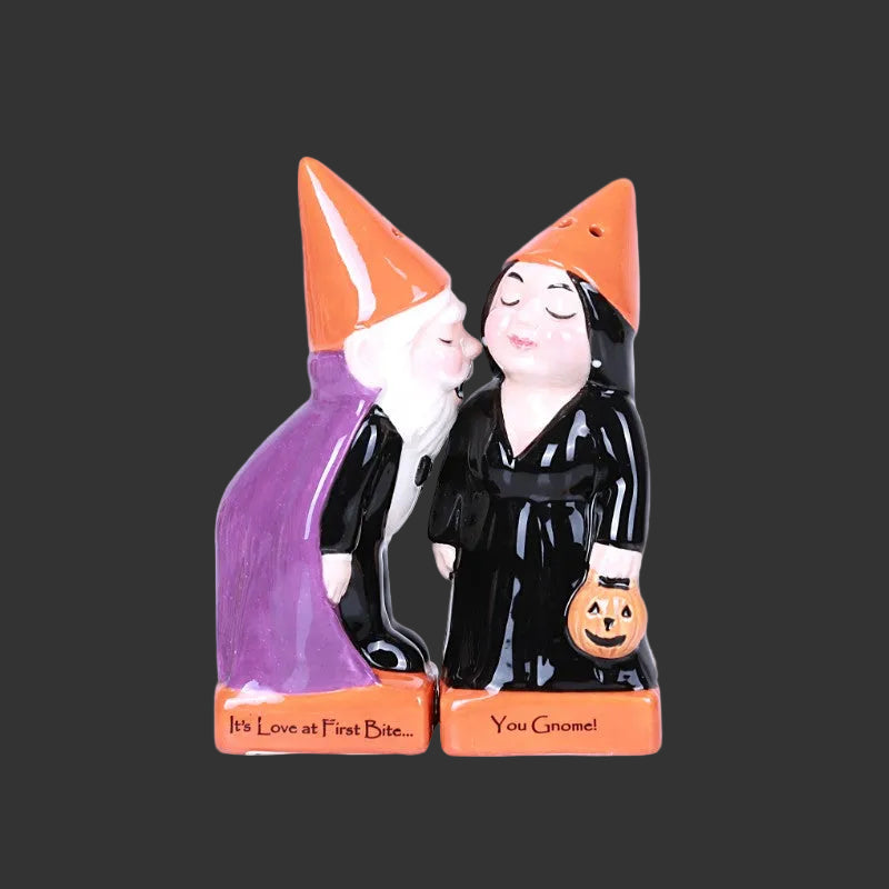 A pair of ceramic Halloween salt and pepper shakers shaped as kissing gnomes. One gnome wears a purple cloak and the other wears a black witch's robe, both with orange pointed hats and standing on orange bases with humorous phrases.