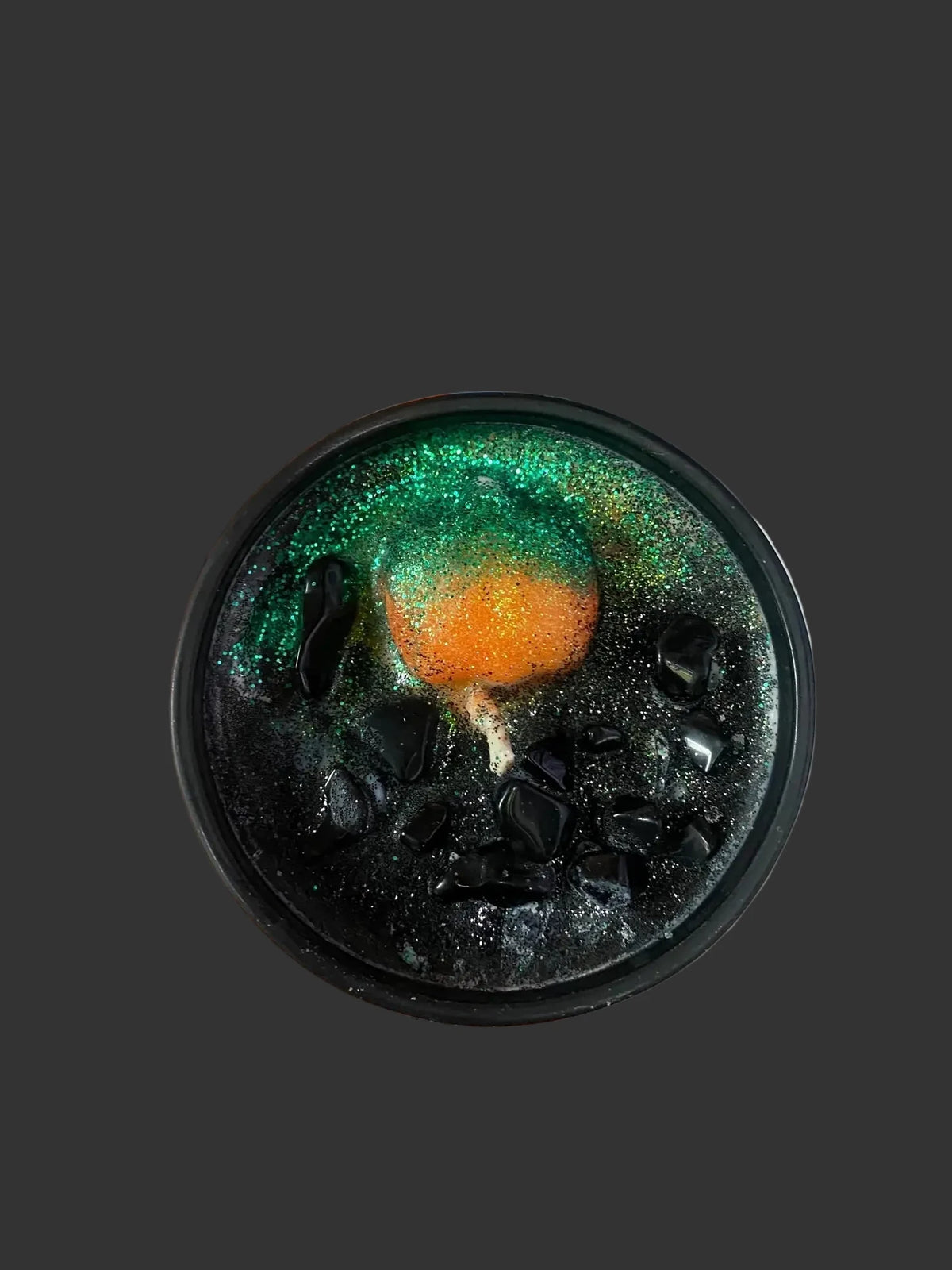 Hand holding a black glittery Halloween container candle with a small pumpkin inside, against a black