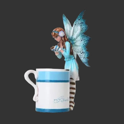 A ceramic mug with a blue and white design, featuring an Amy Brown fairy figurine perched on the side. The mug has a white body with a blue stripe, a blue handle, and a blue logo near the bottom.