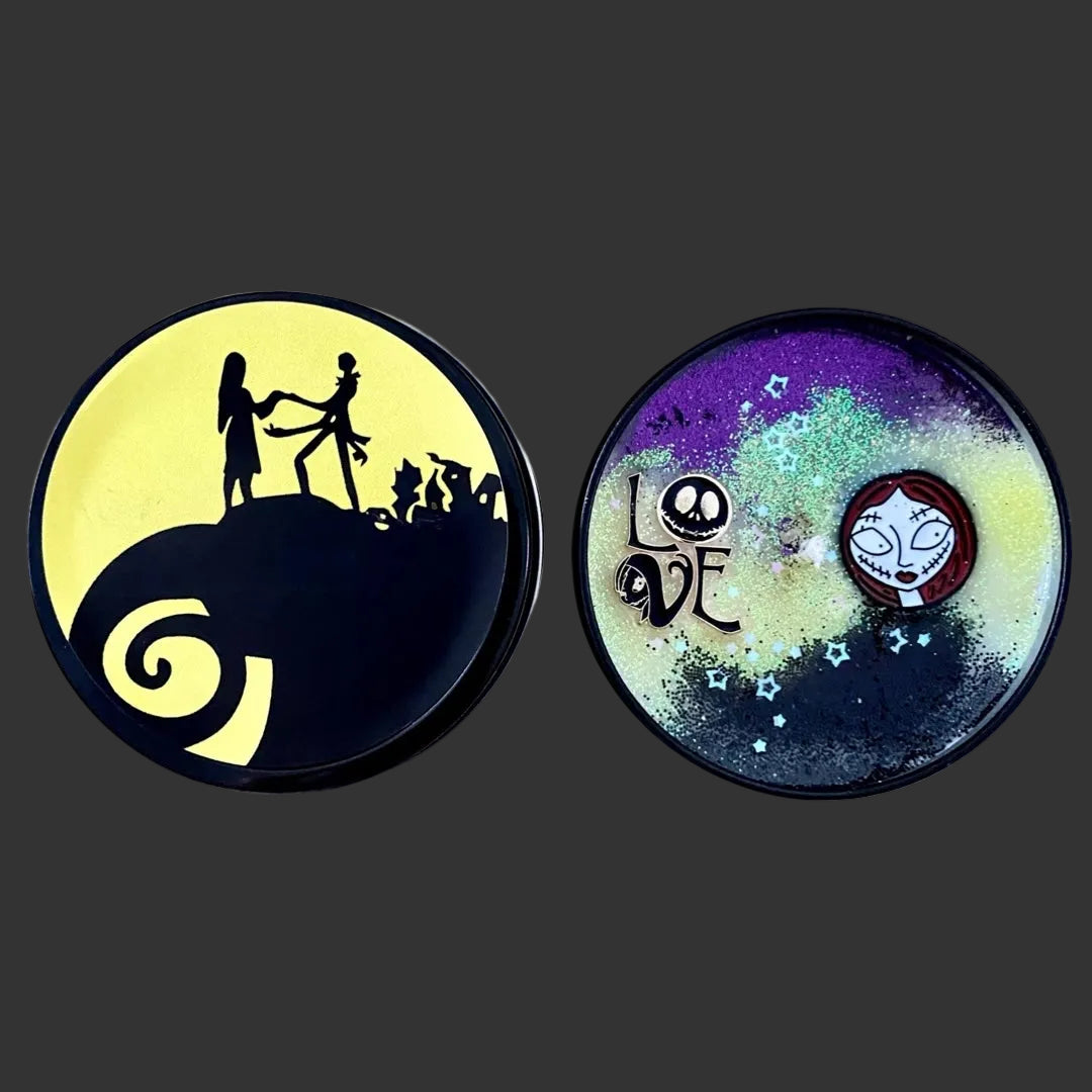 A picture of the candle and tin lid featuring Jack Skellington and Sally from The Nightmare Before Christmas, displayed side-by-side on a black  background. One coaster shows the black silhouette of Jack and Sally on a yellow moon, and the other shows a purple and blue galaxy design with the word 'LOVE' and Sally's face.