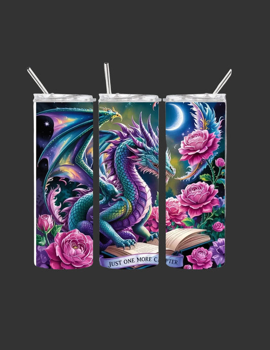 One tall skinny tumblers showing all three sides with clear lids and metal straws, featuring a colorful fantasy illustration of a blue and purple dragon, pink roses, a crescent moon, and an open book on a wood plank background.