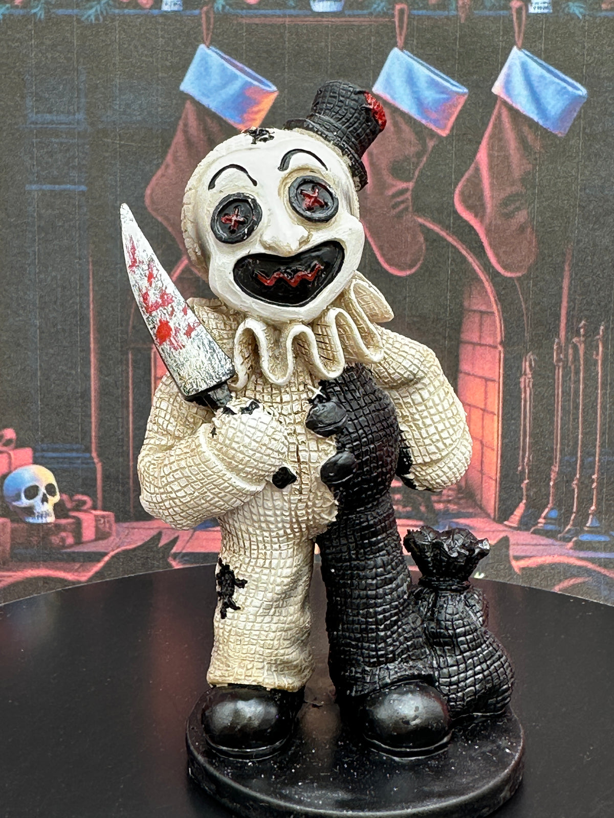 A Creeptoons horror Art the clown figurine standing on a black base, holding a blood-splattered knife and a black sack. The clown has a split design with a textured cream-colored right side and a dark black-left side.