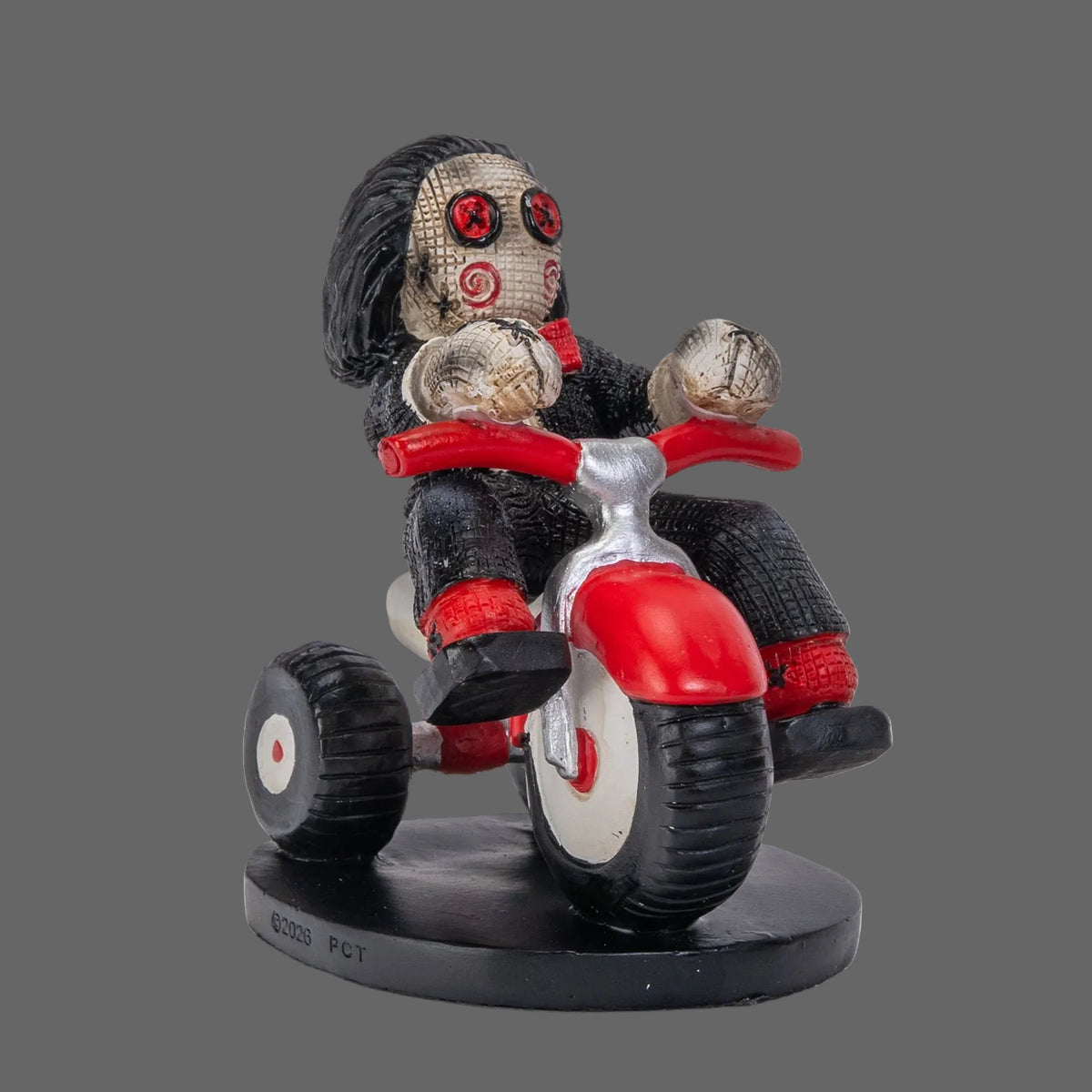 Billy the Puppet Pinhead Monster figurine by Ruben Macias, side angle view showing creepy cute hand-painted resin collectible on red tricycle with button eyes and red bow tie, white background