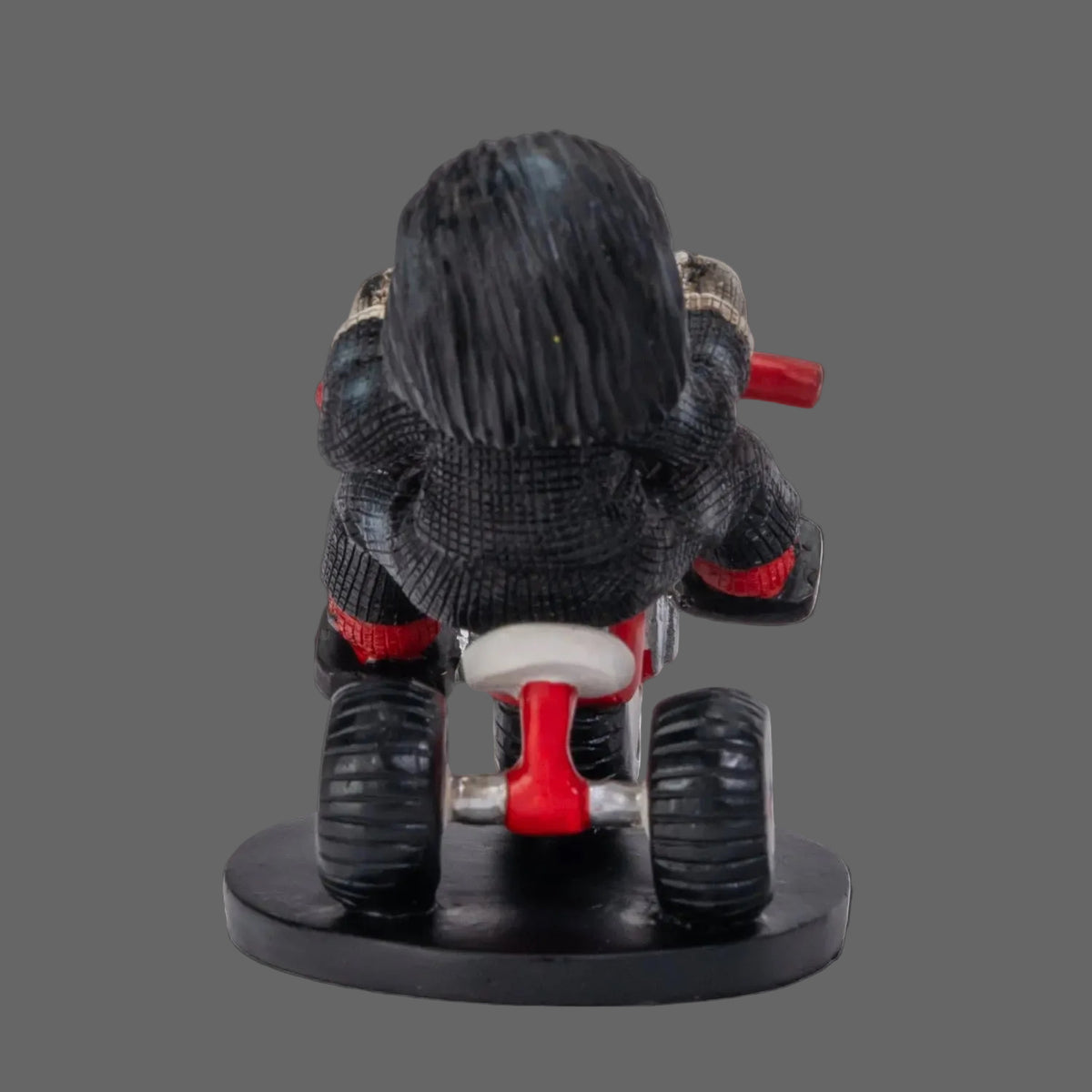 Back view of Billy the Puppet Pinhead Monster figurine showing black hair and red tricycle detail, 2026 Pinhead Monsters collectible by Ruben Macias, shown on black background