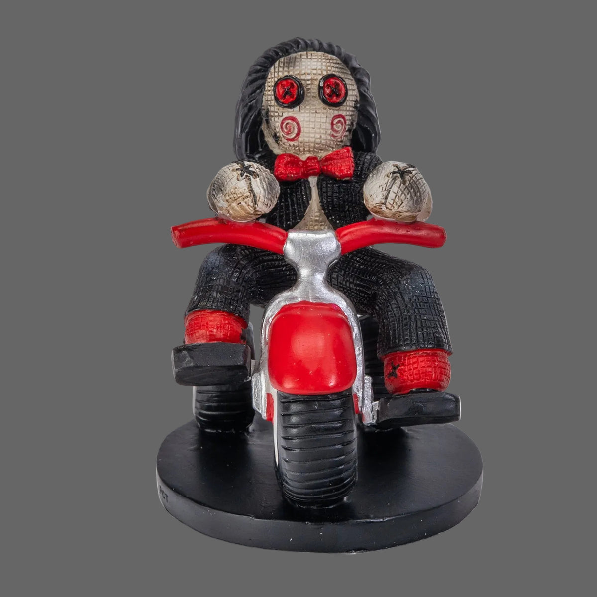 Billy the Puppet Pinhead Monster figurine by Ruben Macias, creepy cute hand-painted resin collectible seated on red tricycle with button eyes and red bow tie, shown on black background