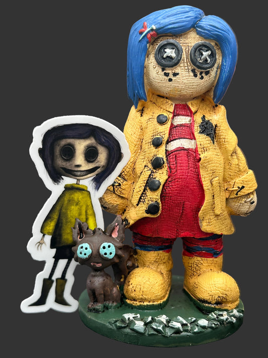 A horror-themed collectible Pinhead Monster Coraline figurine set featuring a creepy blue-haired doll in a yellow coat and red overalls on a green base, alongside a die-cut Creeptoons Coraline sticker and a small brown cat figure with blue eyes.