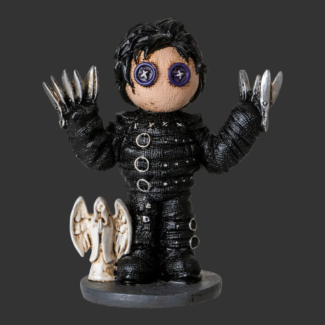 A gothic-style Pinhead Monster collectible Edward Scissorhands figurine with black textured clothing, silver clawed gloves, and purple button eyes, standing on a round base next to a small white angel figure against a black background.