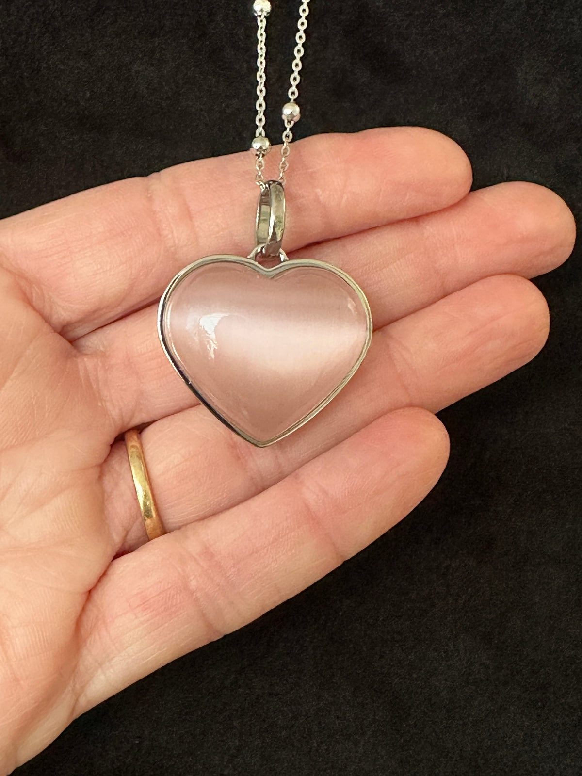 Pink cat eye heart gemstone pendant held in hand showing scale and color