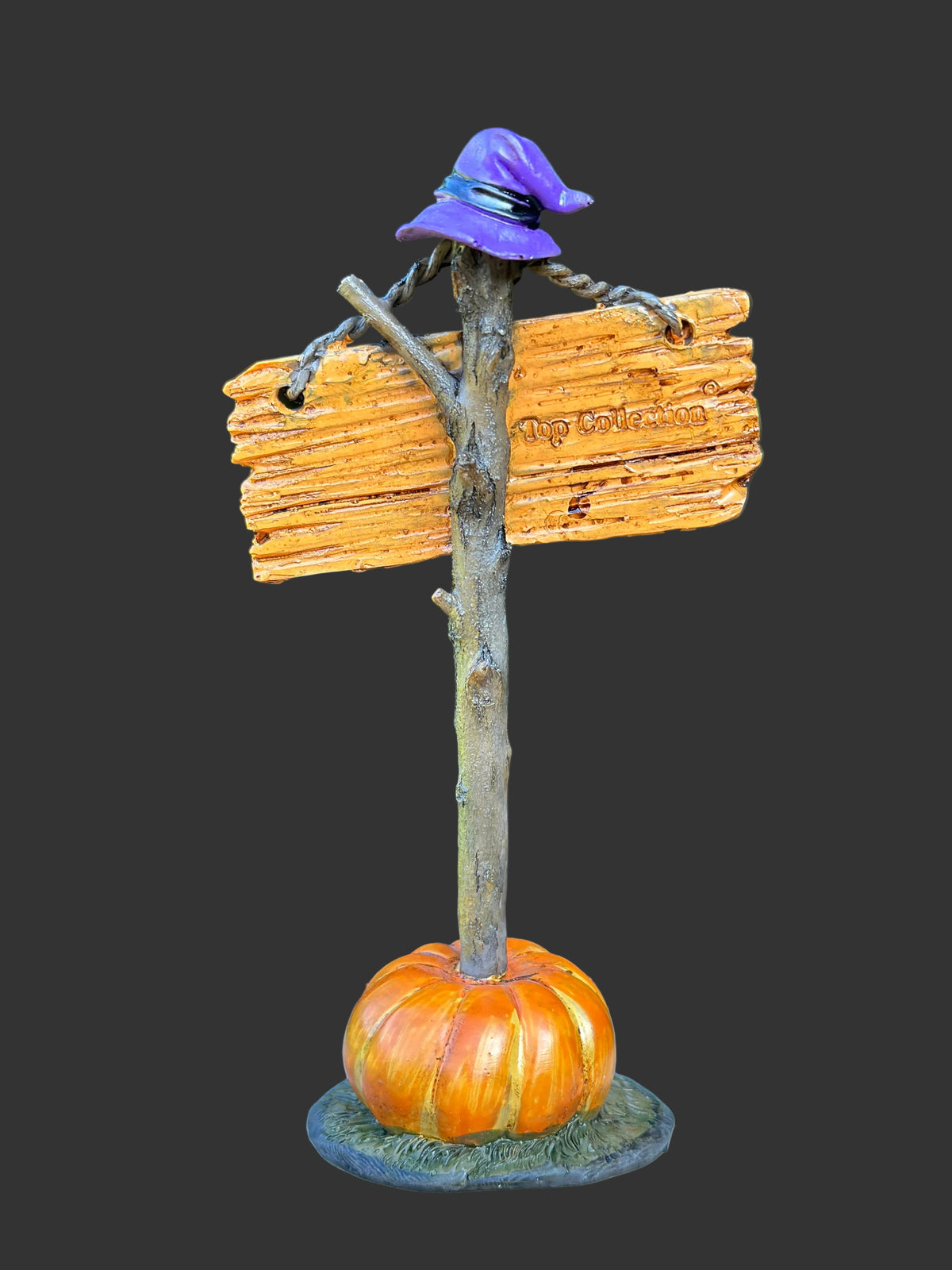Back view of The Witch Is In resin miniature showing purple witch hat on resin twig like post with orange pumpkin base, against dark background