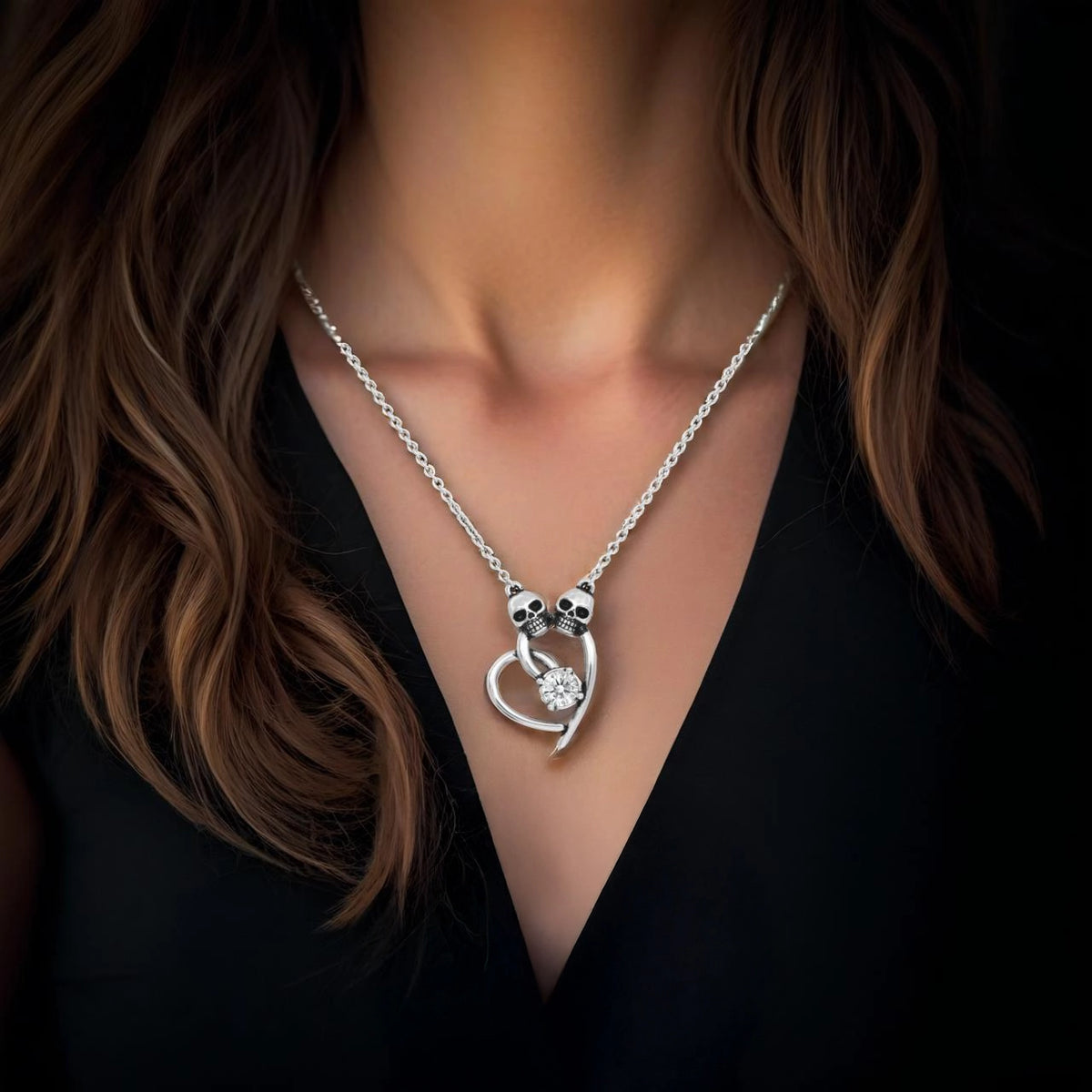 A close-up of a model wearing a silver gothic necklace with a heart-shaped pendant featuring skull details and a clear central gemstone, paired with a black top.