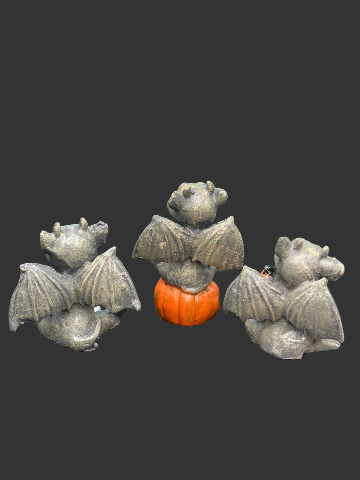 Three miniature gargoyle figurines in a weathered gray finish holding orange pumpkins