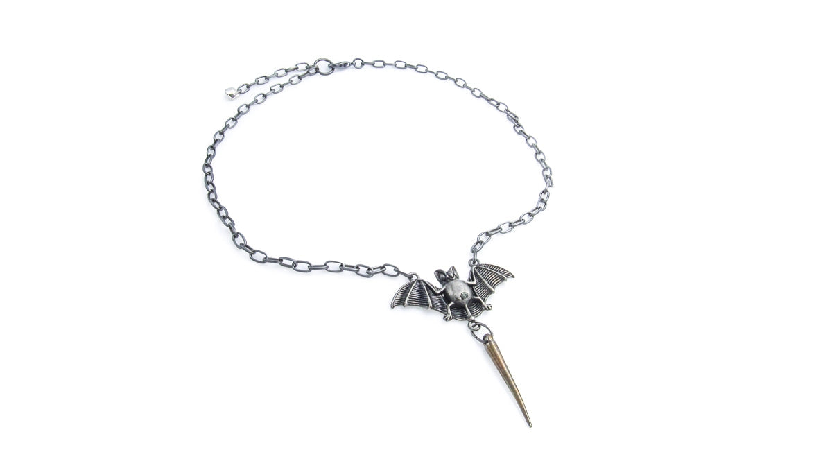 A gothic-style silver chain necklace featuring a small bat pendant with a sharp metallic spike dangling from its tail, displayed on a clean white background.
