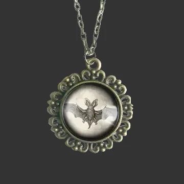 An antique bronze gothic pendant necklace featuring a bat design on a black and white background, suspended from a matching chain against a plain white background.