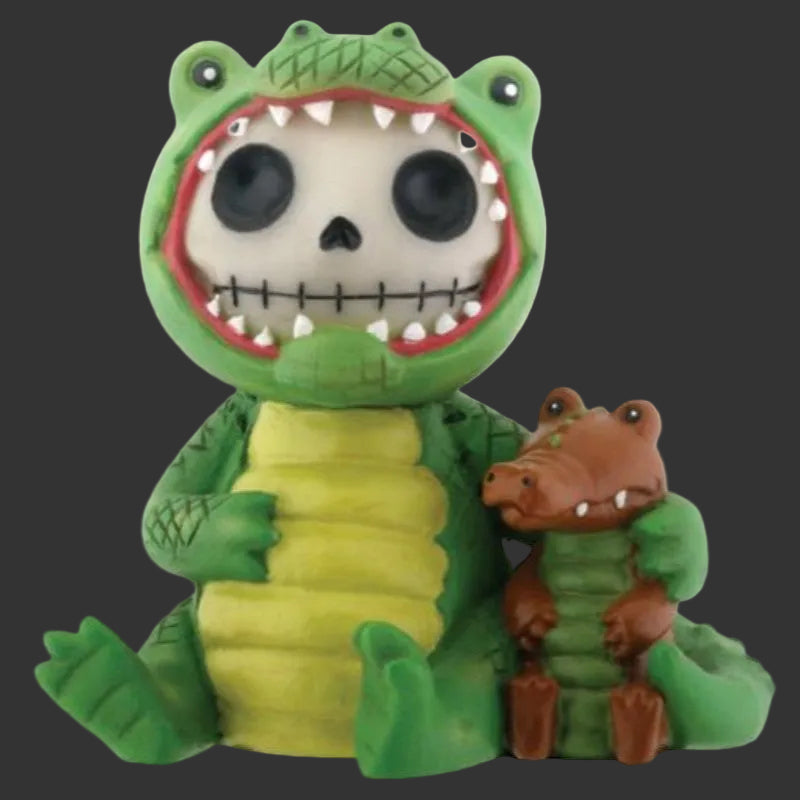 A Furrybones green alligator-themed figurine with a skull face inside its mouth, holding a smaller brown alligator figure, on a plain blackbackground.