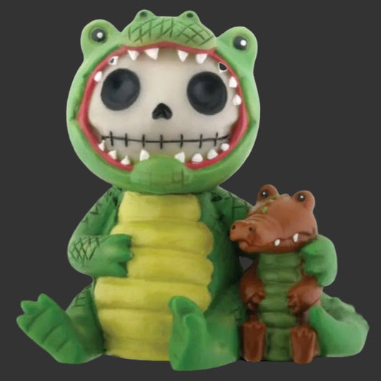 A Furrybones green alligator-themed figurine with a skull face inside its mouth, holding a smaller brown alligator figure, on a plain blackbackground.
