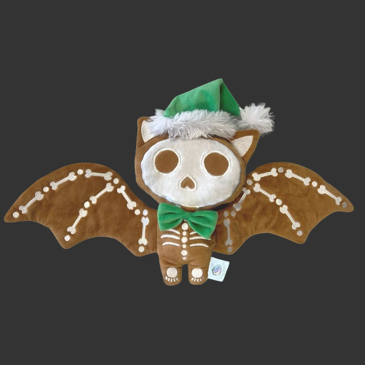 Plush ginger dead holiday bat with skeleton design and green bow and green Santa hat with white fur tie on a black background