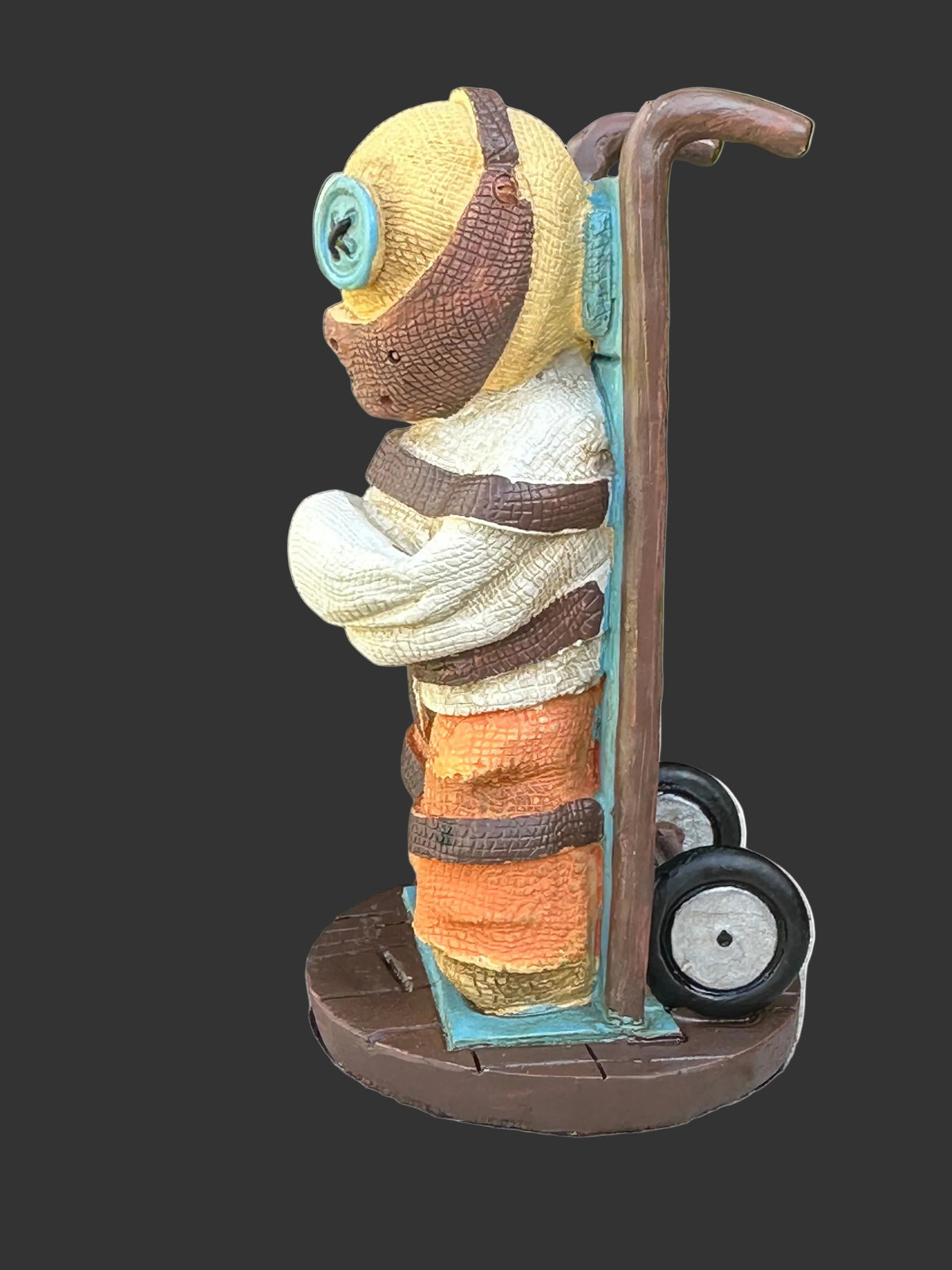 A collectors Pinhead Monster figurine of a Hannibal Lector wearing a white shirt, with orange prison pants and large blue button eyes. He is strapped to a dolly with a mask over his mouth.
