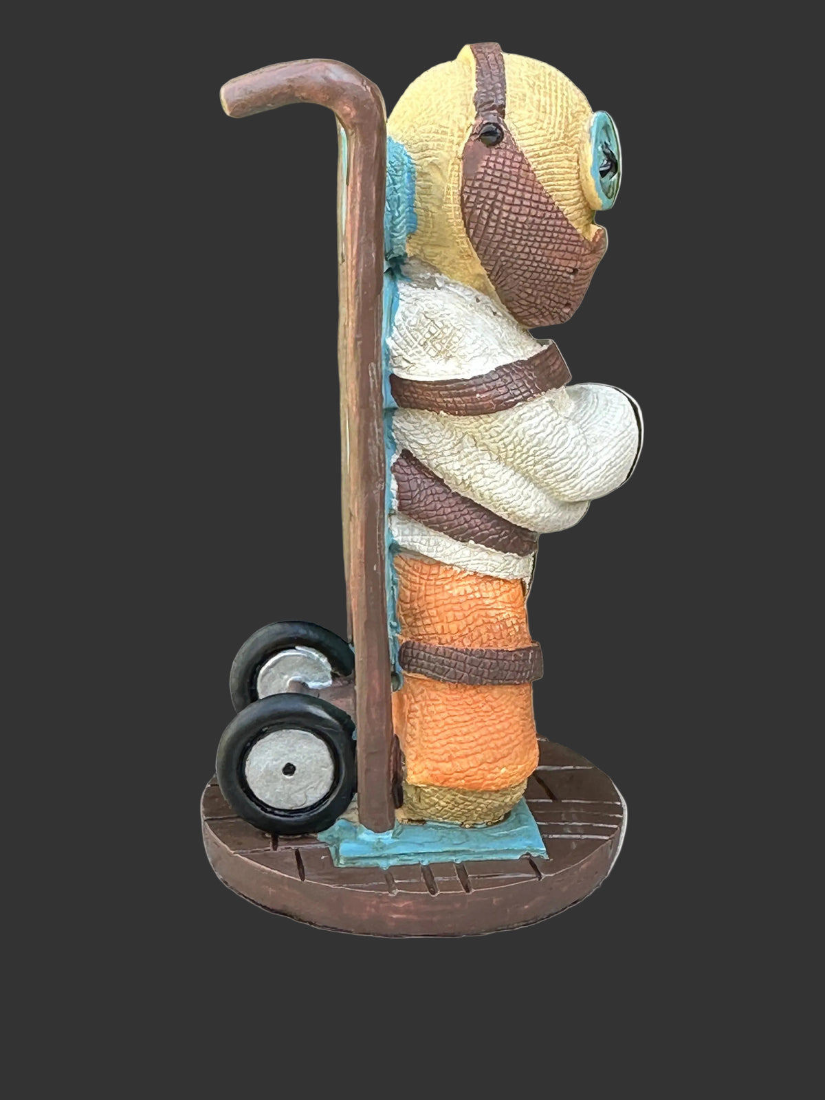 A Pinhead Monster cold cast resin figurine of a Hannibal Lector in a prison suit leaning on a metal trolley, set on a weathered wooden deck.