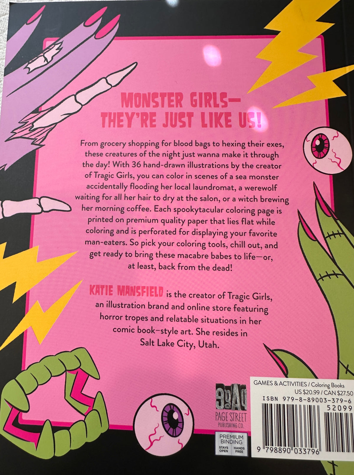 Back cover of a children's coloring book titled 'Monster Girls - They're Just Like Us!' by Katie Mansfield. The cover features a bright pink background with comic-style illustrations of a monster girl, a pink-and-white cat, and a green-and-black spider, along with a barcode and product text.