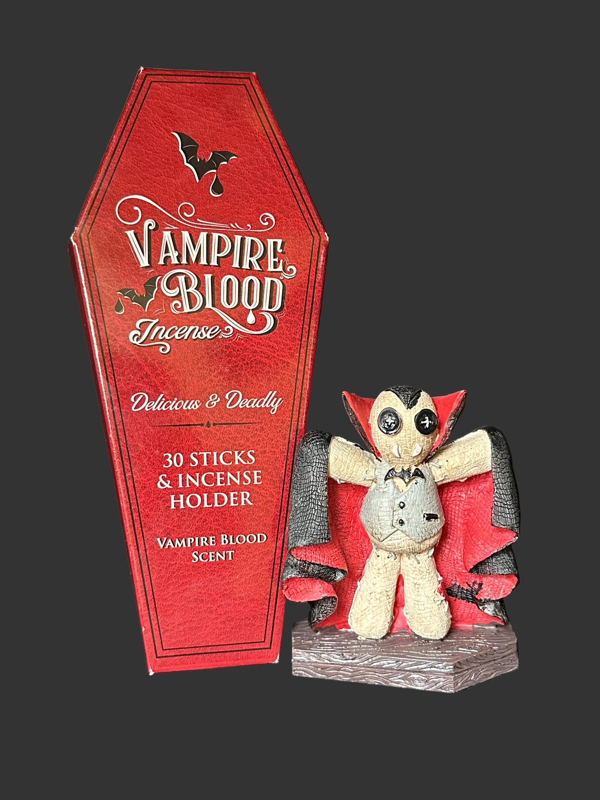 Vampire Blood Incense product display featuring a red coffin-shaped box labeled 'Vampire Blood Incense' next to a small vampire plush toy with red wings and a gray face, set against a dark background.