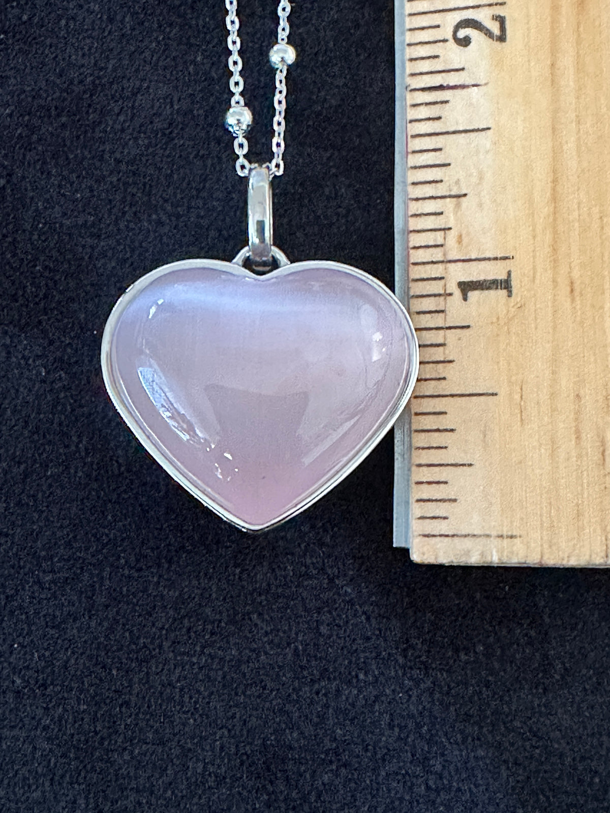 Pink cat eye heart gemstone necklace shown next to a ruler for size reference