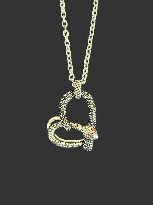 A silver-toned snake pendant necklace with textured scales and small red gemstone eyes, hanging from a matching chain against a dark gray textured background.