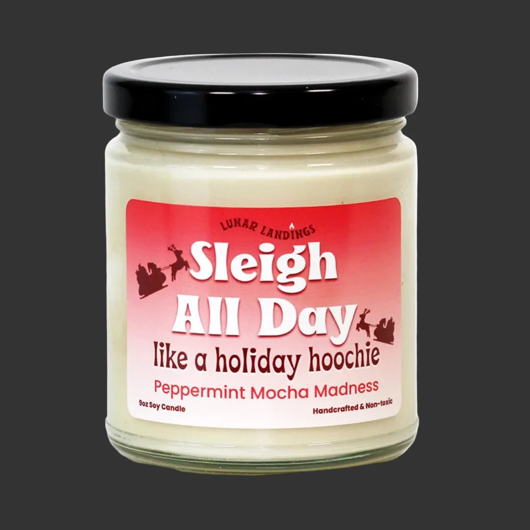 A jar of Lunar Landings 'Sleigh All Day like a holiday hoochie' Peppermint Mocha Madness scented soy candle. The candle is in a clear glass jar with a black lid and a red-to-pink gradient label featuring white and dark red text.