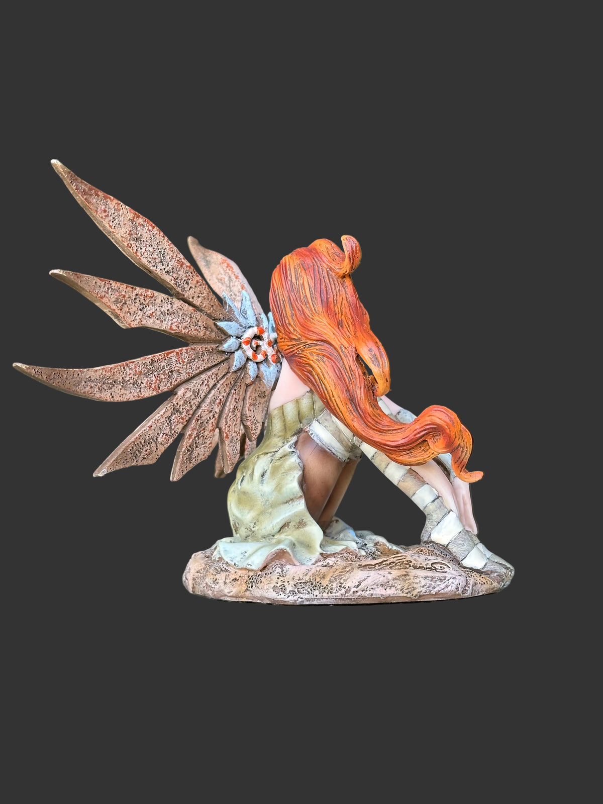 A fantasy winged Amy Brown steampunk fairy figurine with long orange hair, brown wings, and a green dress, posed on a stone surface with green foliage in the background.