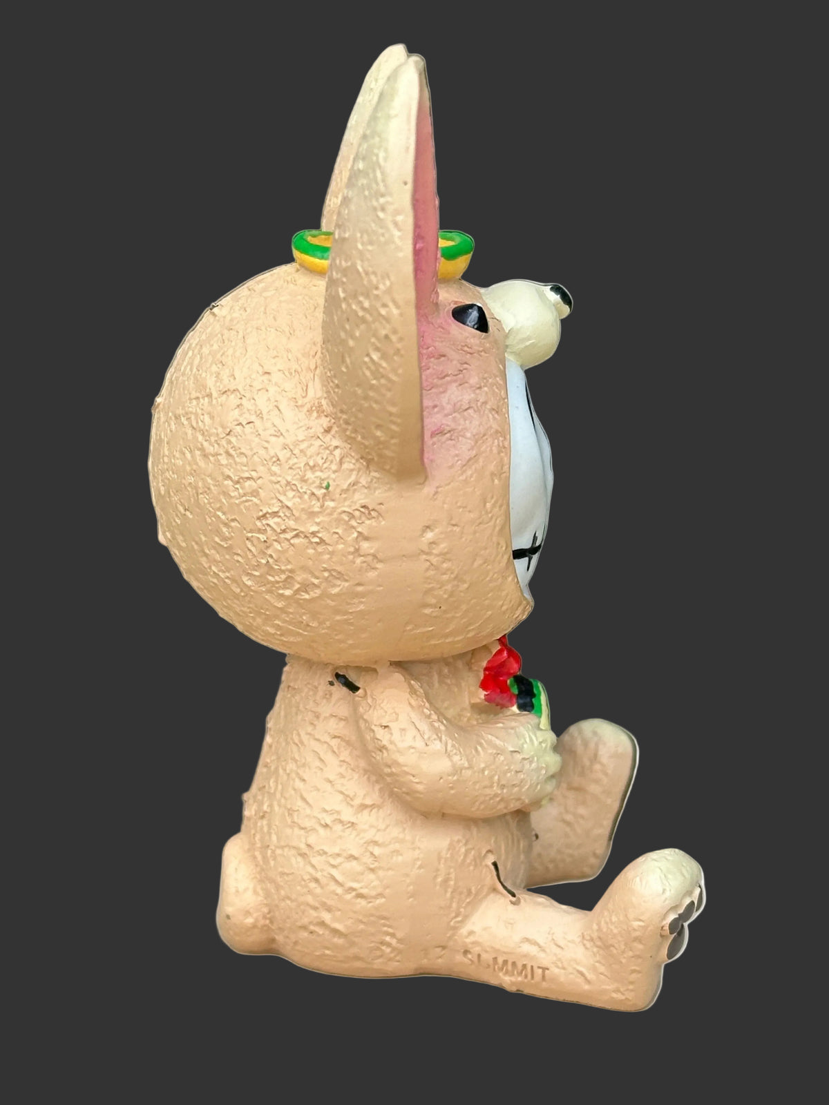 A Furrybones textured beige Chihuahua sitting on a light surface with a blurred green leafy background. The dog has a white face, a small red flower at its chest, and green and yellow accents on its ears.