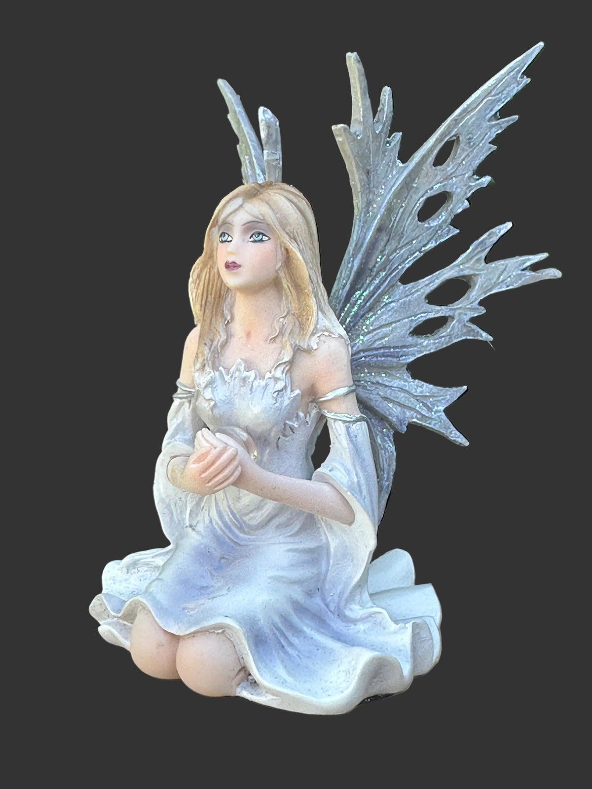A fantasy Dream Eden winter fairy figurine kneeling in a white dress with large iridescent silver wings, shown against a dark gray background.
