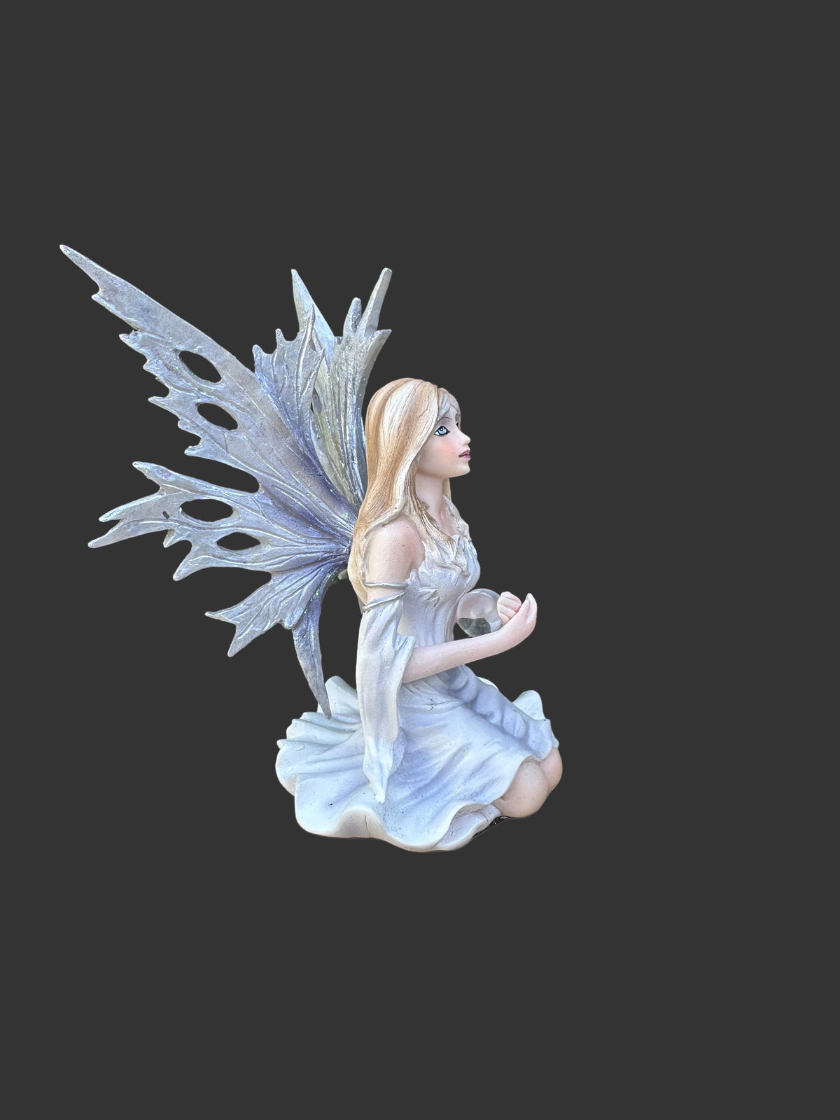 A kneeling Dream Eden winter fairy figurine with large translucent icy wings, long blonde hair, and a white dress, shown against a dark gray background.